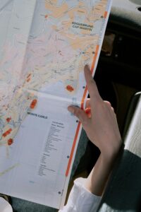 Hand pointing to Monte Carlo on a map in a car, evoking travel and exploration.